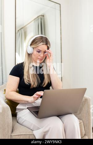 Una donna che lavora intensamente al suo notebook con le cuffie a casa Foto Stock