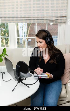 Podcasting e appunti di una donna concentrata durante la registrazione a casa Foto Stock