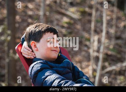 Un ragazzo felice che si rilassa su una sedia all'aperto in un giorno di primavera. Foto Stock