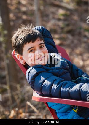 Primo piano di un ragazzo sorridente che si rilassa su una sedia all'aperto in un giorno di primavera. Foto Stock