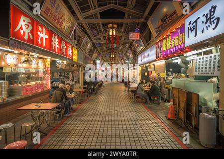 Un vivace mercato notturno si snoda con vivaci cartelli, bancarelle diverse e persone che si godono l'atmosfera Foto Stock