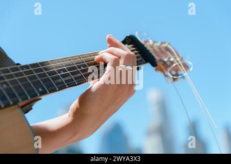 Primo piano di mani sulla chitarra collo di un chitarrista che fa accordi suonare musica per strada facendo musica con il cielo in sottofondo. copia spazio. Foto Stock