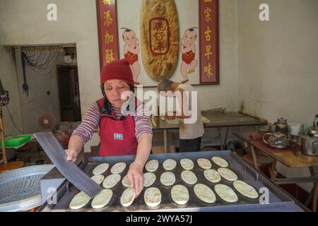 Una coppia di anziani che prepara il pane in un piccolo negozio con un cartello cinese Foto Stock