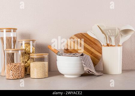 Due grandi ciotole in ceramica, un set di barattoli per alimenti sfusi, un set di utensili da cucina su un ripiano in pietra. Bellissimo sfondo della cucina. Vista frontale. Cucina ecologica. Foto Stock