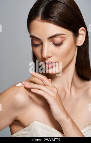 Una giovane donna con i capelli bruna posa graziosamente in un abito senza spalline, le sue mani toccano delicatamente la crema sulla spalla Foto Stock