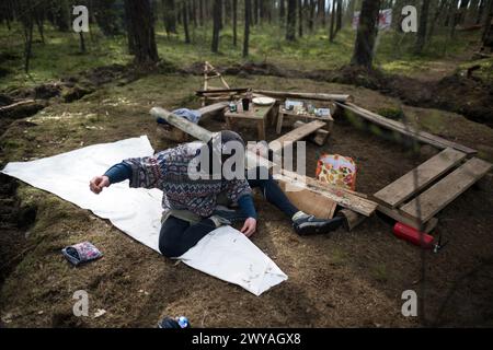 5 aprile 2024, Brandeburgo, Grünheide: Un attivista cuce una tela cerata nel campo dell'iniziativa "Tesla SToppen" in una pineta vicino alla fabbrica Tesla Gigafactory Berlino-Brandeburgo. Gli attivisti del campo di protesta contro l'espansione Tesla a Grünheide si stanno preparando per un'occupazione più lunga della foresta. Foto: Sebastian Christoph Gollnow/dpa Foto Stock