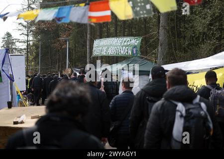 5 aprile 2024, Brandeburgo, Grünheide: I dipendenti Tesla passano davanti a una veglia con uno striscione che recita "l'occupazione dell'acqua saluta i lavoratori" vicino a un campo dell'iniziativa "Stop Tesla" in una pineta vicino alla Gigafactory Tesla Berlino-Brandeburgo. Gli attivisti del campo di protesta contro l'espansione Tesla a Grünheide si stanno preparando per un'occupazione più lunga della foresta. Foto: Sebastian Christoph Gollnow/dpa Foto Stock