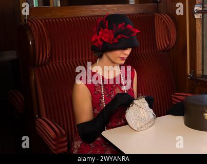 Attraente donna 1920s in abito flapper rosso e cappello di cloche posa nel 1927 prima classe interno di un autentico treno a vapore Foto Stock