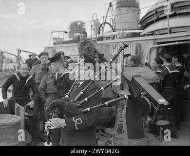 GRANDE IMPRESA INGEGNERISTICA BRITANNICA: PORTI PREFABBRICATI (MULBERRY). DAL 6 ALL'8 GIUGNO, A BORDO DEL PIROSCAFO A PALE HMS ARISTOCRAT DURANTE IL PASSAGGIO ATTRAVERSO IL CANALE E L'ARRIVO AD ARROMANCHES, DOVE IL MULBERRY AVANZAVA IL PORTO E IL GRUPPO SBARCARONO. - Il sottotenente A Mitchell, RNVR, di Glasgow, ufficiale elettrico della HMS ARISTOCRAT, la gioca sulle cornamuse mentre lascia la nave deposito HMS DISPATCH per salpare per la Normandia. , Foto Stock