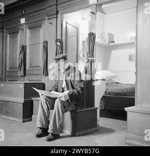 ROYAL HOSPITAL CHELSEA: VITA DI TUTTI I GIORNI CON I PENSIONATI DI CHELSEA, LONDRA, INGHILTERRA, Regno Unito, 1945 - Un pensionato di Chelsea si siede su un petto per leggere il giornale fuori dal suo "ormeggio" o cubicolo su uno dei Long Wards del Royal Hospital Chelsea. Secondo la didascalia originale "ogni pensionato è responsabile di mantenere il proprio armadio ordinato e pulito, tranne in caso di disabilità quando lo fa l'infermiere del reparto!". , Foto Stock