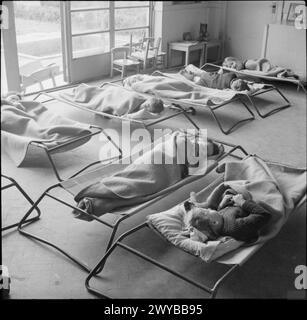 Una SCUOLA DI VILLAGGIO MODERNO: EDUCAZIONE NEL CAMBRIDGESHIRE, INGHILTERRA, Regno Unito, 1944 - i bambini piccoli dormono in piccoli "letti da campeggio" alla Bottisham Nursery School, Cambridgeshire. Secondo la didascalia originale, il riposo di metà giornata fa parte della... routine. Il benessere fisico dei bambini è una preoccupazione primaria dell'istruzione moderna”. La camera ha finestre francesi, molte delle quali sono aperte per far entrare aria fresca. , Foto Stock