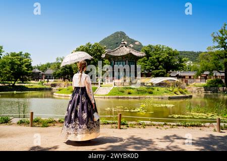 Seoul, Corea del Sud. Hanbok che indossa una donna. Giardino del parco del palazzo Gyeongbokgung. Tradizione coreana dell'abbigliamento. Padiglione Hyangwonjeong sullo sfondo. Foto Stock