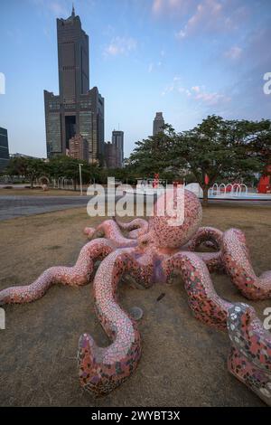 Un'intricata scultura gigante di polpo si estende per il terreno con un moderno paesaggio urbano che si erge alle spalle Foto Stock