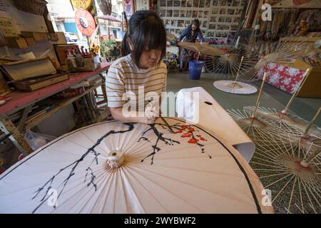 In un laboratorio, un artista decora un ombrello di carta con intricati disegni floreali Foto Stock