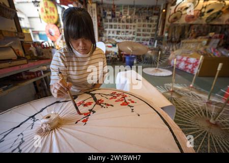 In un laboratorio, un artista decora un ombrello di carta con intricati disegni floreali Foto Stock