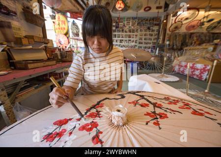 In un laboratorio, un artista decora un ombrello di carta con intricati disegni floreali Foto Stock