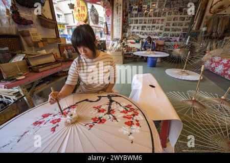 In un laboratorio, un artista decora un ombrello di carta con intricati disegni floreali Foto Stock