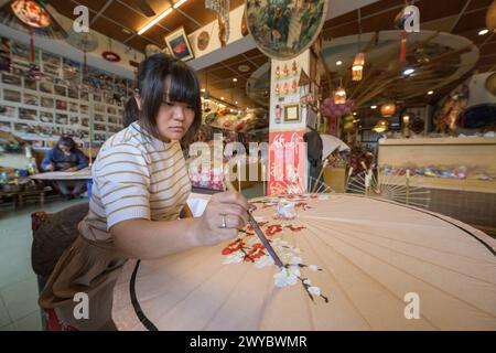 In un laboratorio, un artista decora un ombrello di carta con intricati disegni floreali Foto Stock