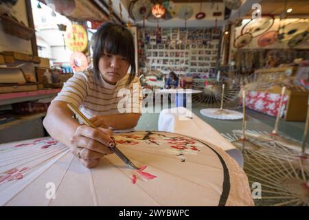 In un laboratorio, un artista decora un ombrello di carta con intricati disegni floreali Foto Stock