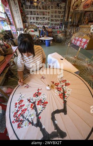 In un laboratorio, un artista decora un ombrello di carta con intricati disegni floreali Foto Stock