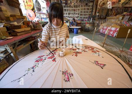 In un laboratorio, un artista decora un ombrello di carta con intricati disegni floreali Foto Stock