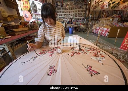 In un laboratorio, un artista decora un ombrello di carta con intricati disegni floreali Foto Stock