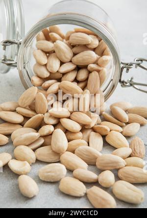 Spuntino con noci di mandorle sbucciate bianche crude in vaso di vetro sul tavolo da cucina bianco. Foto Stock