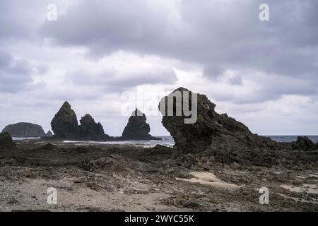 I cieli moscosi si infrangono su un feroce paesaggio marino con grandi formazioni rocciose e onde turbolente che si infrangono contro di loro Foto Stock