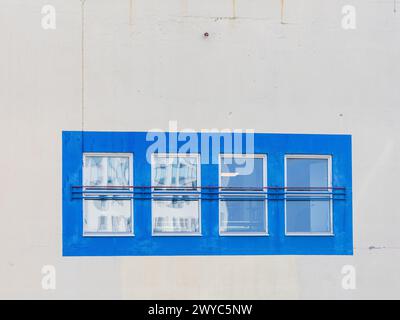 Una fila di quattro finestre collocate in una cornice blu brillante contrasta nettamente con la facciata pallida minimalista di un edificio. Ogni finestra riflette una differenza Foto Stock