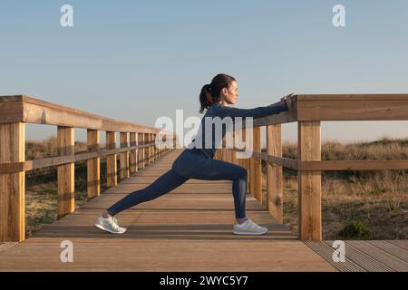 Indossate una donna sportiva che fa esercizi di stretching su una passerella di legno Foto Stock