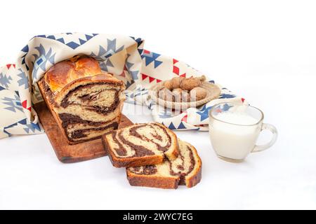 Cozonac, tradizionale pane dolce rumeno con ripieno di noci, tagliato a fette, con un bicchiere di latte e stoffa a motivi geometrici, vista laterale isolata Foto Stock