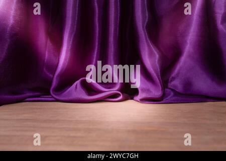 Pavimento in legno vuoto con eleganti tende in raso viola ondulato, sfocate sullo sfondo, sfondo del posizionamento dei prodotti Foto Stock