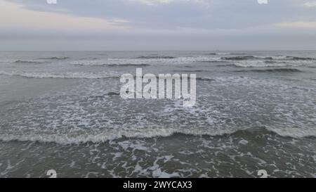 La marea dell'oceano in arrivo incontra la spiaggia sabbiosa sotto le nuvole di raccolta Foto Stock