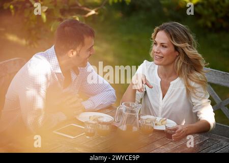 In coppia, all'aperto o a cena con tablet e sorriso al tramonto, conversazione per relazione o matrimonio. Donna, uomo o fuori a tavola per Foto Stock