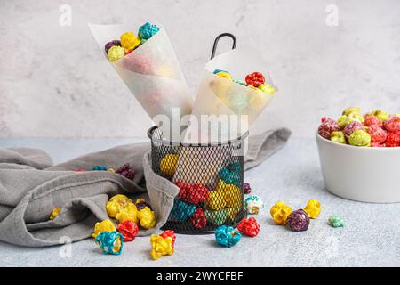 Coni di carta con pop corn colorati e dolci in un cestello per frittura profonda su un tavolo bianco Foto Stock