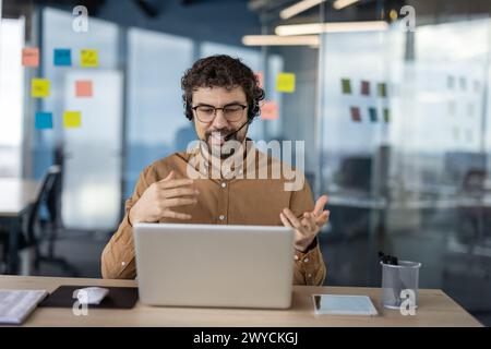 Uomo d'affari ispanico che indossa una cuffia e partecipa a una videochiamata in un ufficio moderno. Foto Stock