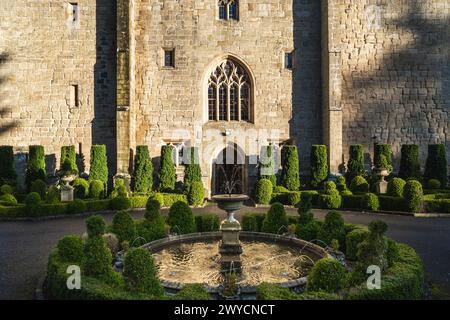 Il giardino formale e la porta d'ingresso di uno storico castello con fontana ornata e alberi topiari ben rifiniti Foto Stock