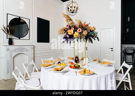 Un sofisticato tavolo da pranzo con accenti dorati e un sontuoso centrotavola floreale in un ambiente interno di lusso. Foto Stock