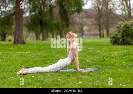 Donna che fa yoga in parco, esercizio di cobra. Foto Stock