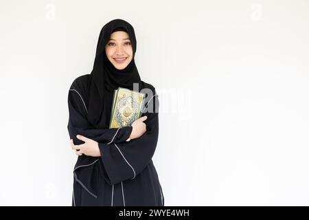 Ritratto felice musulmano saudita niqab donna araba chador nero con il libro del Santo al Corano isolato sul bianco. Copertina del libro calligrafia araba tradotta in A. Foto Stock