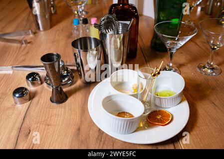 Un set di preparazione per cocktail con agitatori in acciaio inox, jigger e una varietà di agrumi su un tavolo da bar in legno. Foto Stock