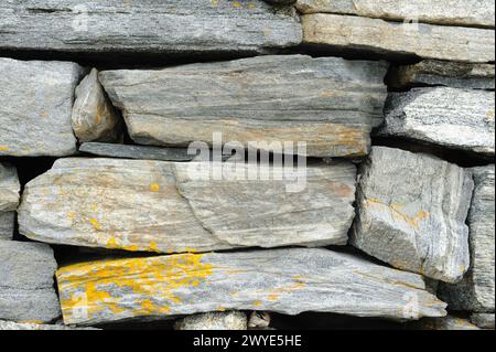 Una vista dettagliata di un muro di pietra a secco con pietre grigie a incastro e macchie di lichene giallo. Foto Stock