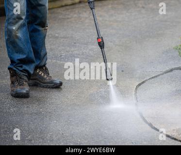 Operaio che pulisce la pavimentazione utilizzando un getto d'acqua elettrico. Foto Stock