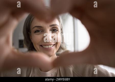 Allegra donna piuttosto anziana mostra un gesto del cuore guardando la fotocamera Foto Stock
