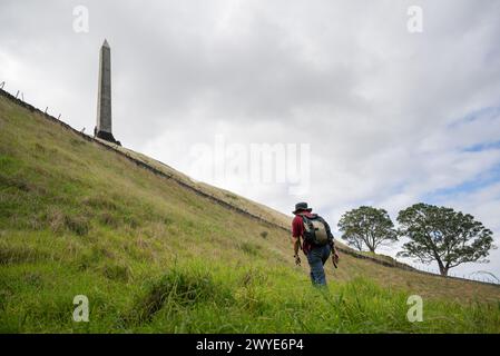 Uomo che cammina in salita verso l'obelisco sulla cima di One Tree Hill. Auckland. Foto Stock