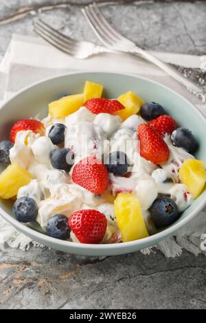 Deliziosa cheesecake, insalata di frutta e bacche con fragole, mirtilli, ananas in primo piano in una ciotola su un tavolo di marmo. Verticale Foto Stock