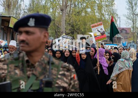 Un trooper paramilitare indiano sta in guardia mentre le donne musulmane tengono cartelli e recitano slogan contro Israele e l'America durante una protesta contro le operazioni militari israeliane a Gaza. Decine di musulmani del Kashmir hanno portato cartelli e bandiere palestinesi durante una manifestazione nel Magam centrale del Kashmir a circa 25 km da Srinagar, commemorando il giorno di al-Quds (Gerusalemme). La giornata di al-Quds è osservata a livello globale l'ultimo venerdì (Jumat-ul-Vida) del mese Santo del Ramadan per esprimere solidarietà e sostegno ai palestinesi. (Foto di Faisal Bashir/SOPA Images/Sipa USA) Foto Stock