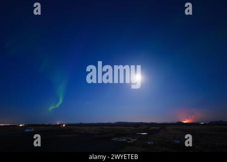 L'aurora boreale e l'eruzione vulcanica durante l'ora Blu con la Luna piena nel cielo notturno alla penisola di Reykjanes in Islanda Foto Stock