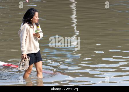 SAMUT PRAKAN, TAILANDIA, 11 febbraio 2024, Una donna sorridente aspetta attraverso una strada allagata Foto Stock