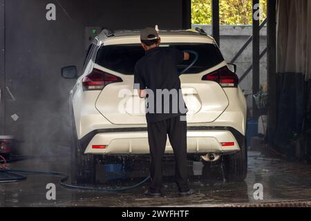 Un uomo lava un'auto con un tubo flessibile di pressione all'interno di una stazione di servizio Foto Stock